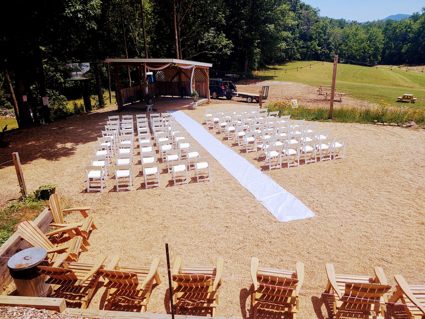 Outdoor wedding ceremony set with white chairs and an aisle leading to a flower-draped arbor